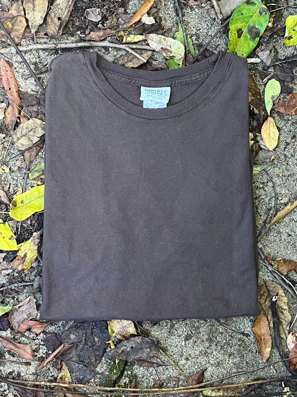 Natural Bark Brown Organic cotton T-shirt on a ground surface with leaves