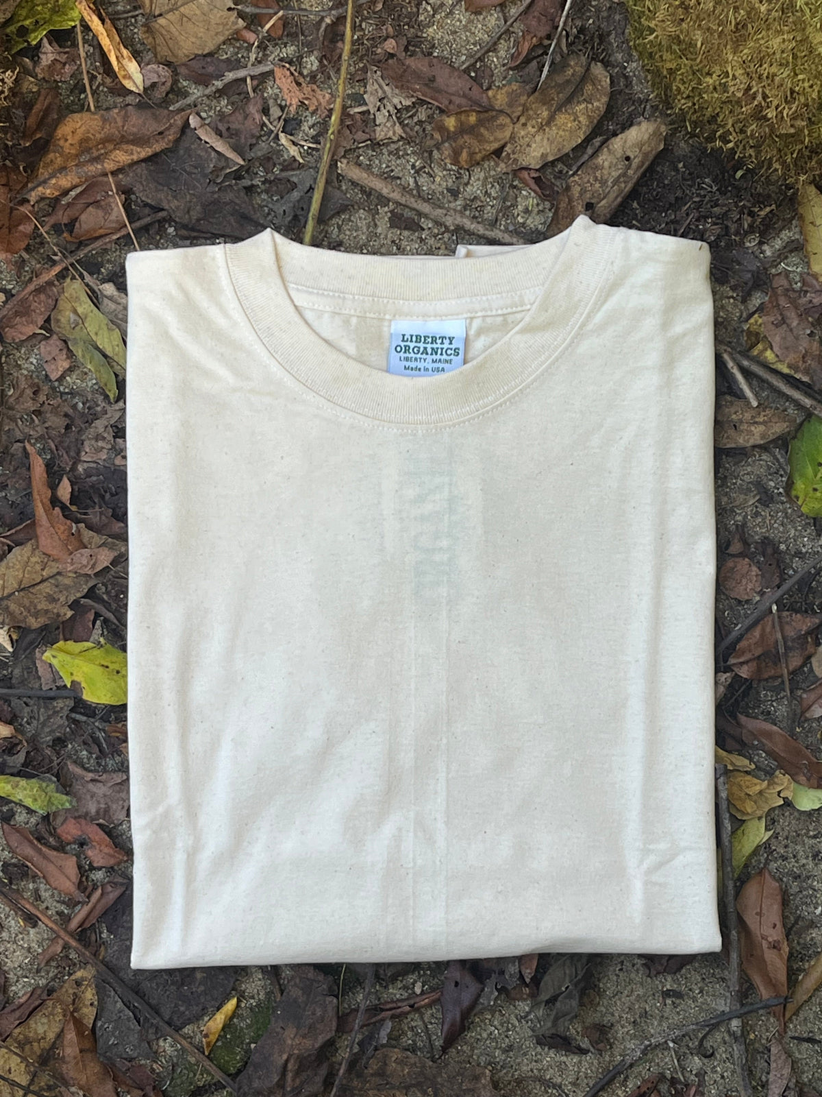Organi cotton natural White t-shirt on a ground surface with leaves